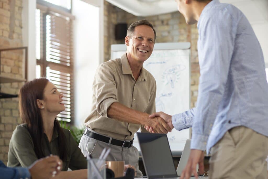 A man smiles and shakes hands with a new SIBN member in a meeting room